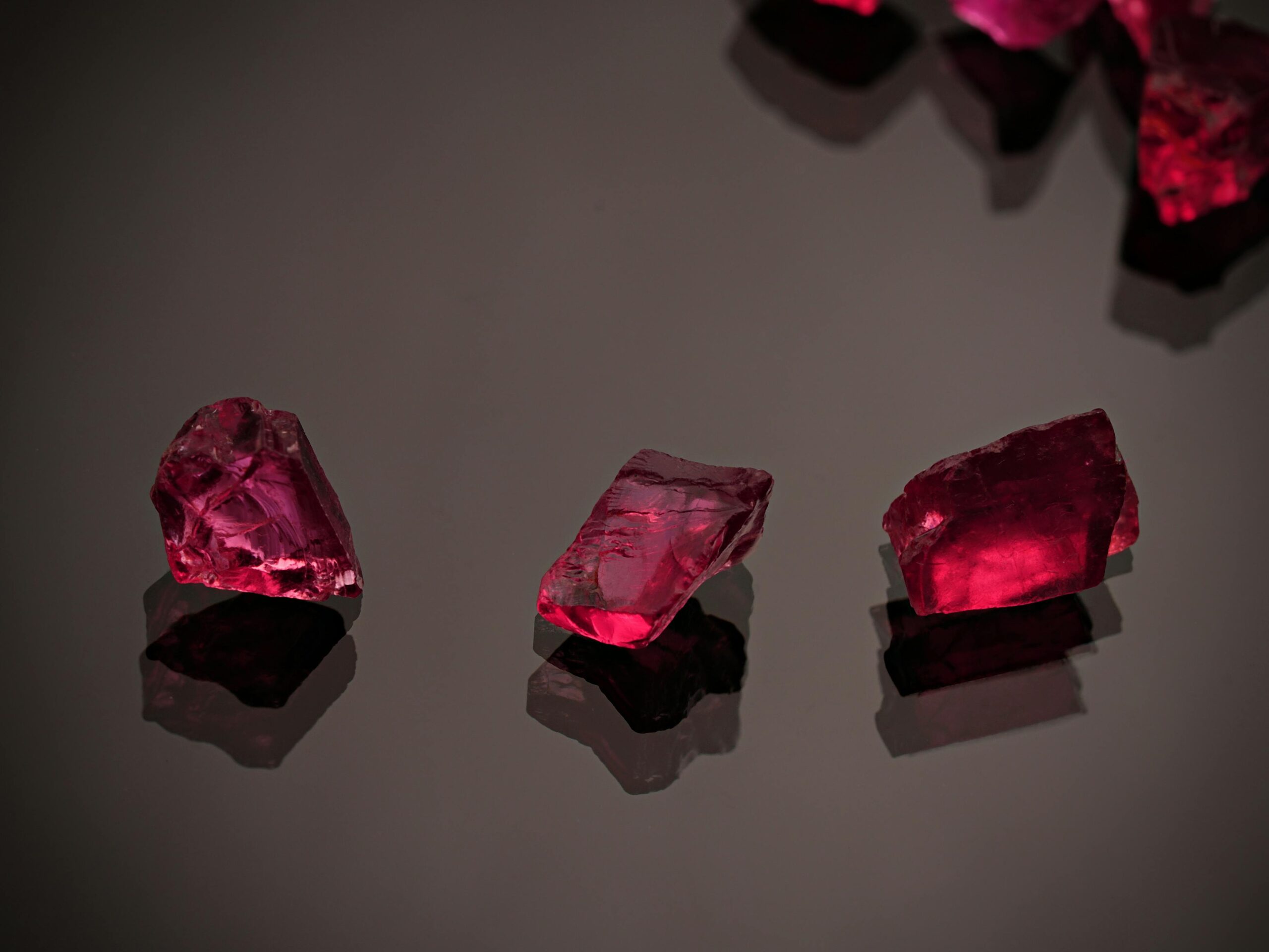 Three red gemstones glitter against a dark reflective background in a still life composition.