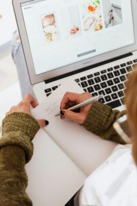 Overhead view of a woman writing in a notebook while browsing on a laptop.