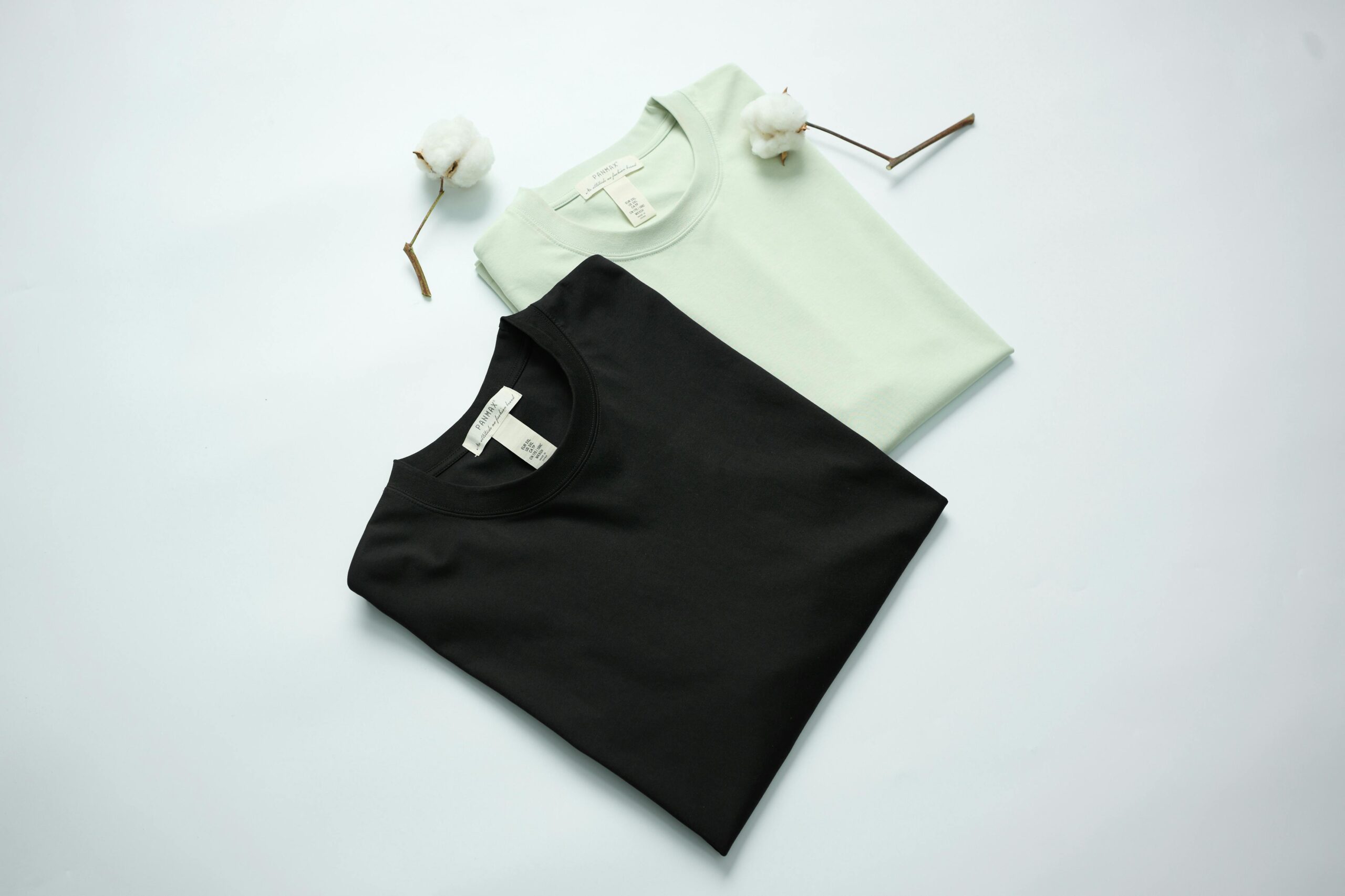 Two cotton t-shirts in black and mint green on a light background with cotton flowers.